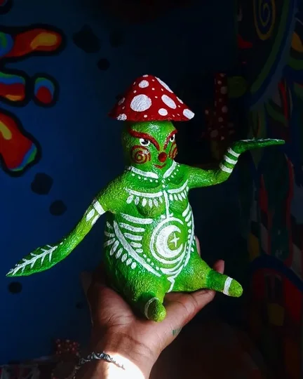 Escultura verde de criatura com chapéu de cogumelo vermelho