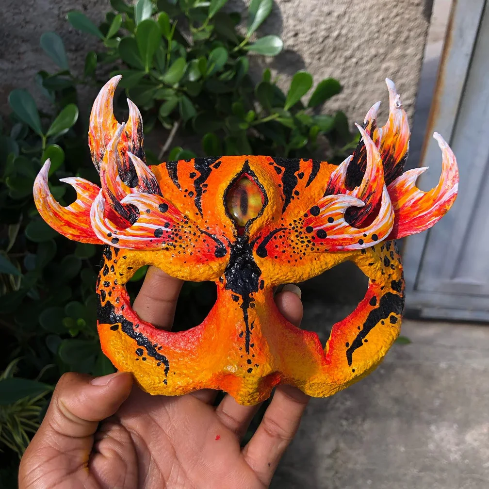 Máscara artesanal laranja inspirada na fênix, com chamas esculpidas