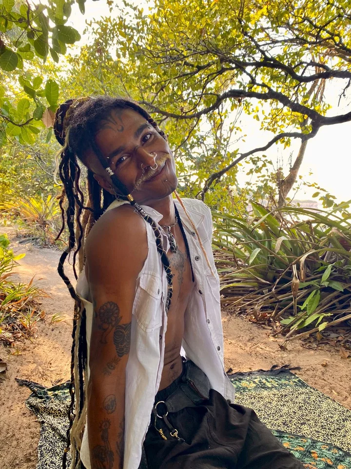 Lerísc Art em retrato, entre árvores, com dreads e colete claro